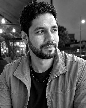Retrato en blanco y negro de Diego Antunes, un hombre con barba y chaqueta de lona, en la terraza de un café al anochecer